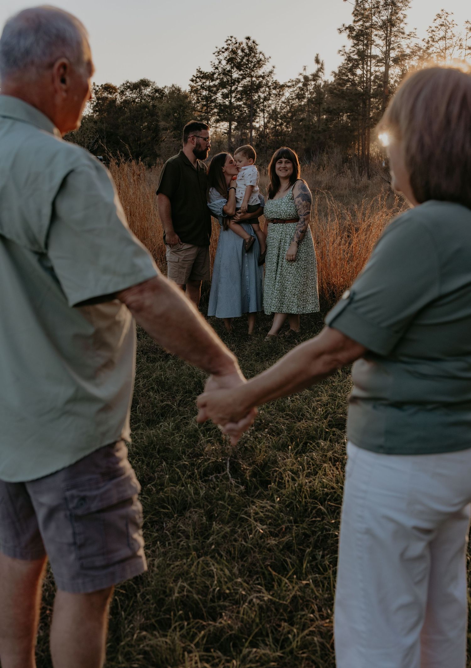 Family playing together in tall grass field during golden hour.