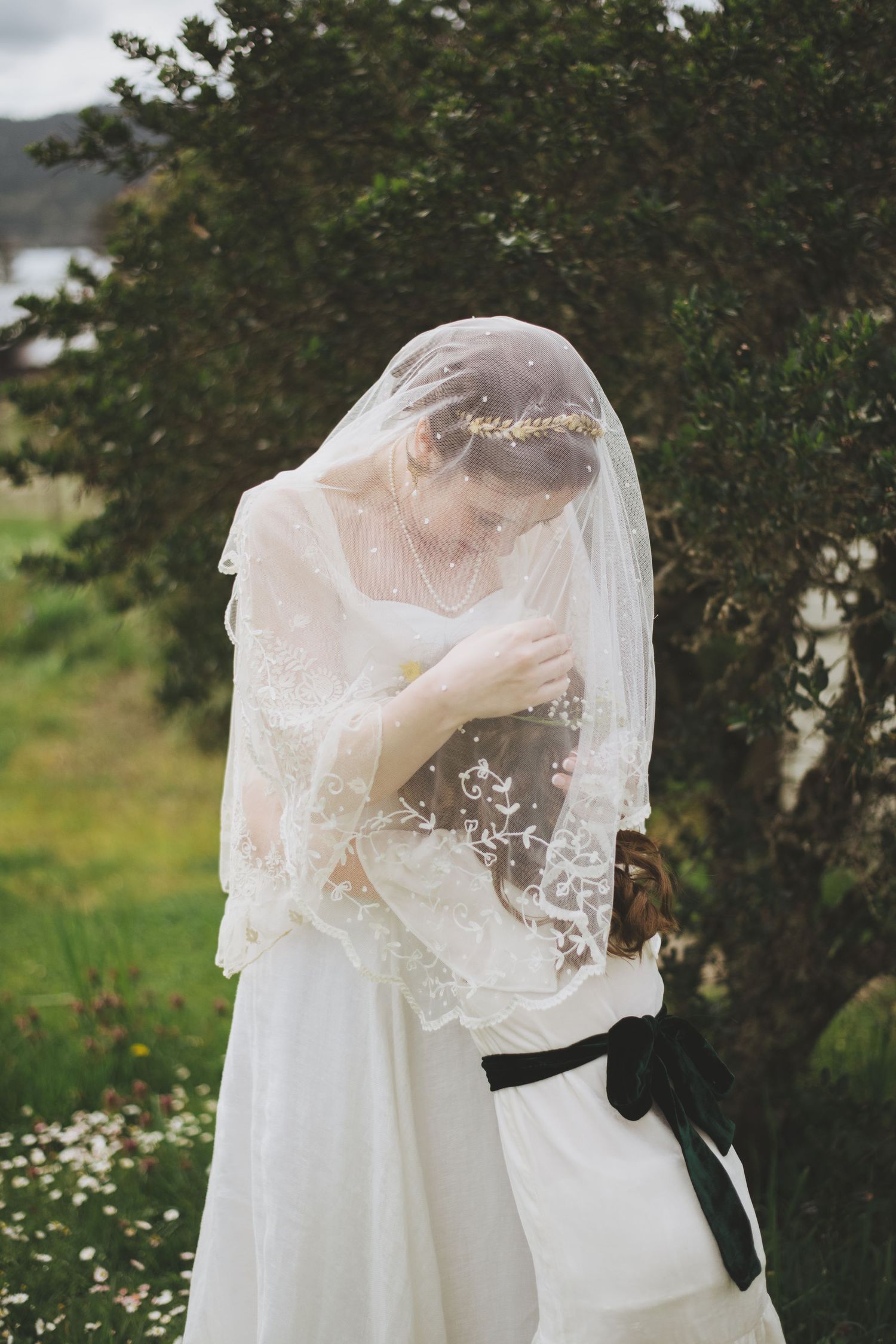 A delicate lace wedding veil drapes over a white wedding dress in an outdoor garden setting.