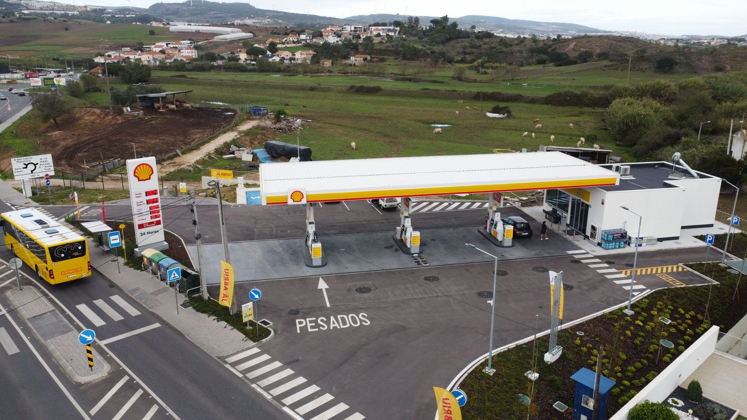 Aerial view of a Shell fuel station with yellow canopy, pumps, and bus stop at road junction.
