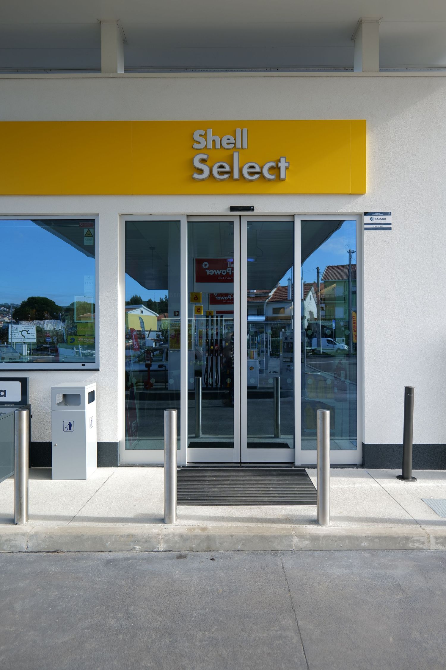 Shell Select convenience store entrance with automatic glass doors and yellow branded signage above.