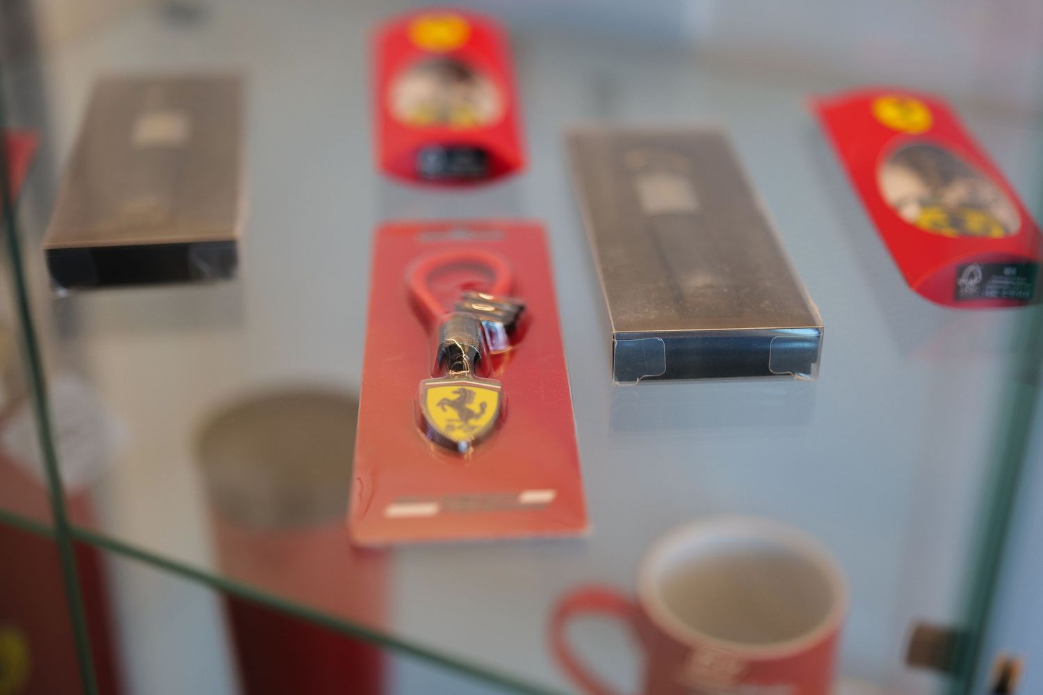 Ferrari branded keychains and phone cases displayed on a glass shelf in a store.