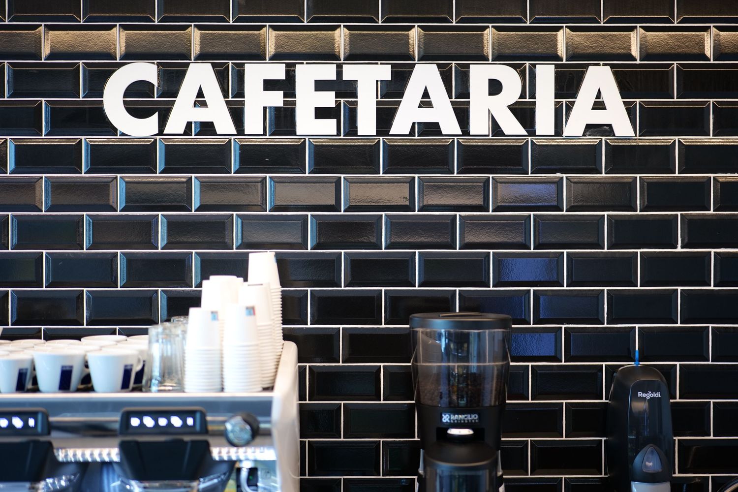 Cafetaria sign on black brick wall above espresso machine and coffee supplies.