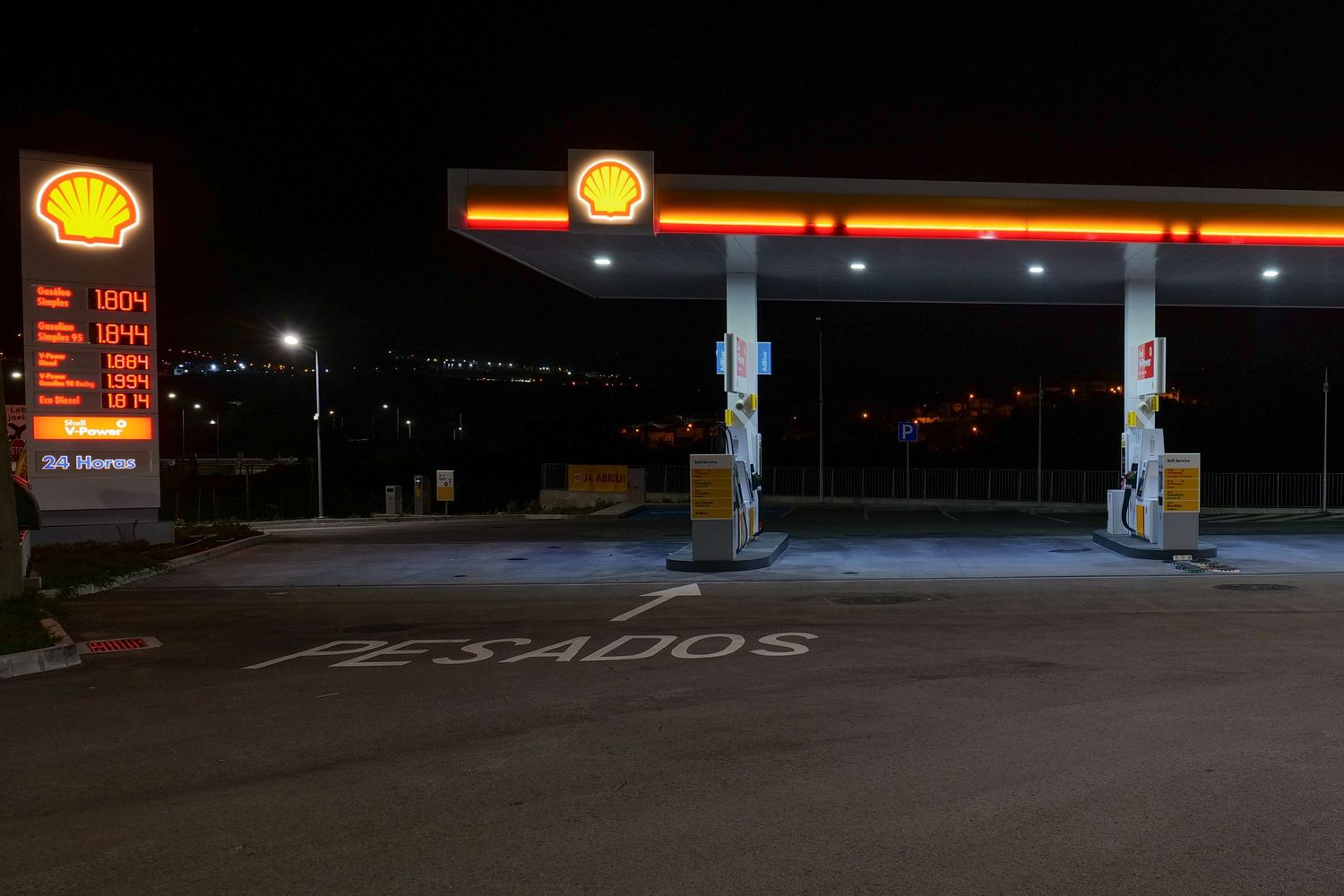 Shell gas station illuminated at night with price sign and PESADOS marked pavement.