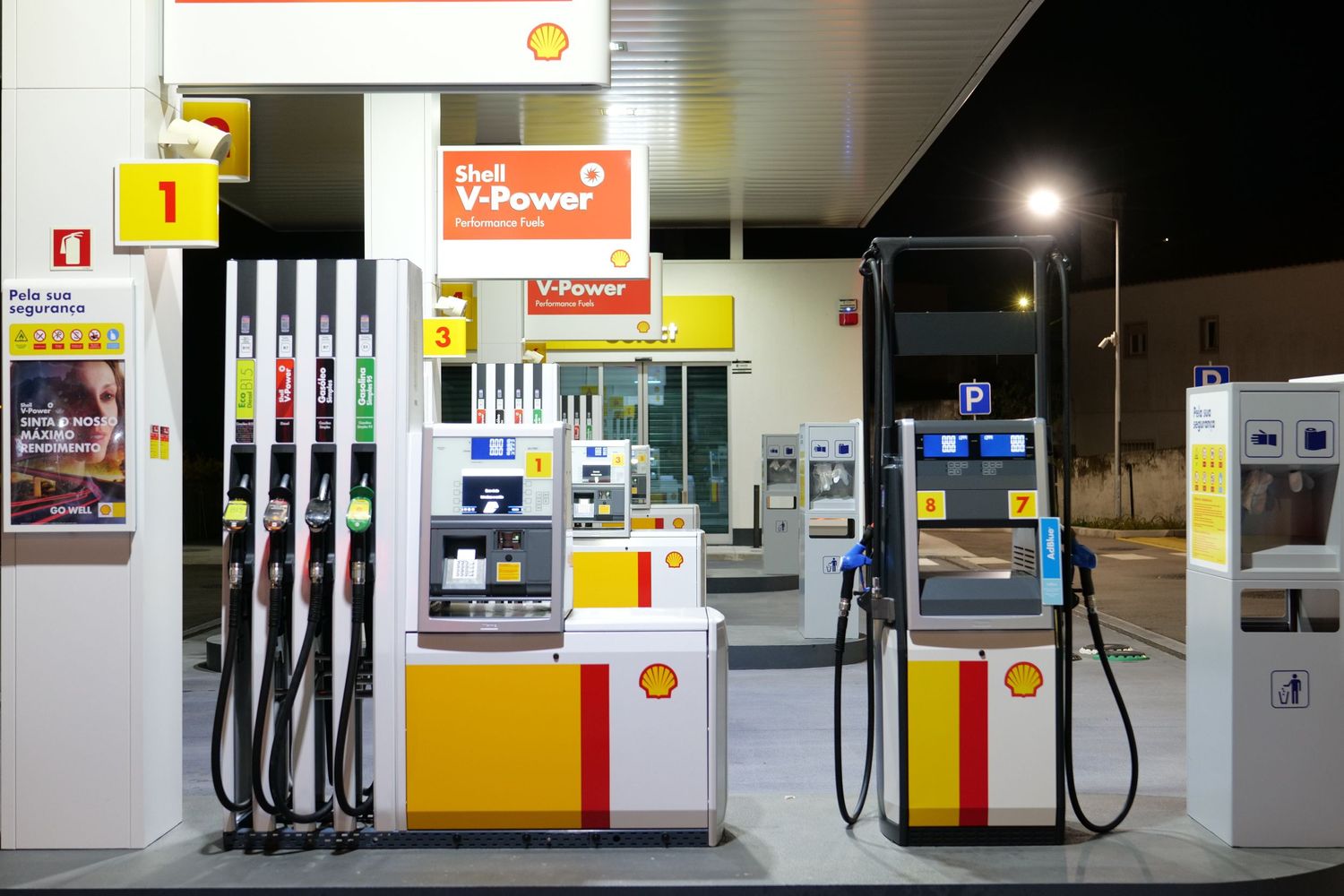 Shell V-Power gas station with multiple fuel dispensers and payment terminals illuminated at night.