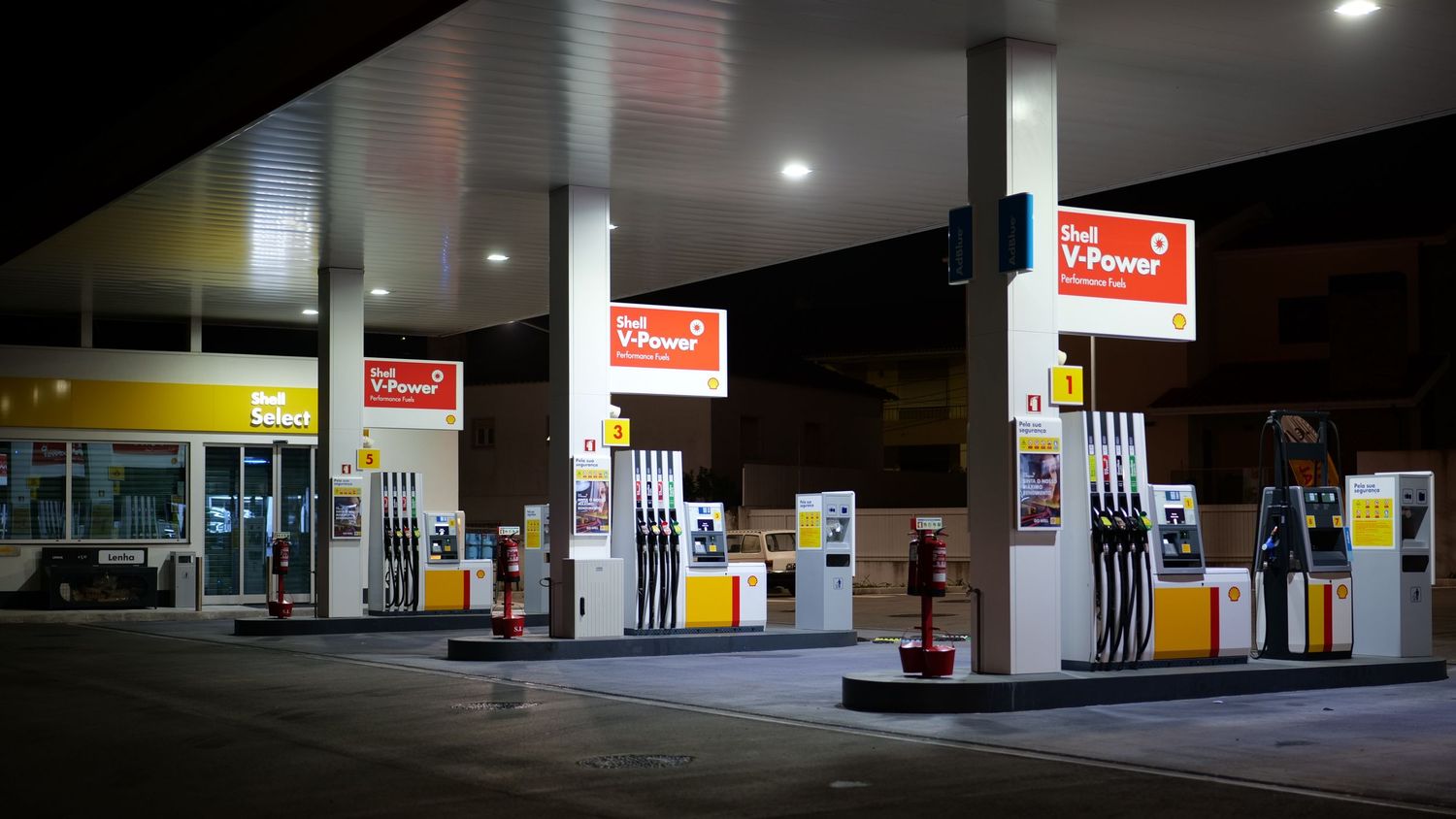 Shell gas station illuminated at night with fuel pumps under bright canopy lights.