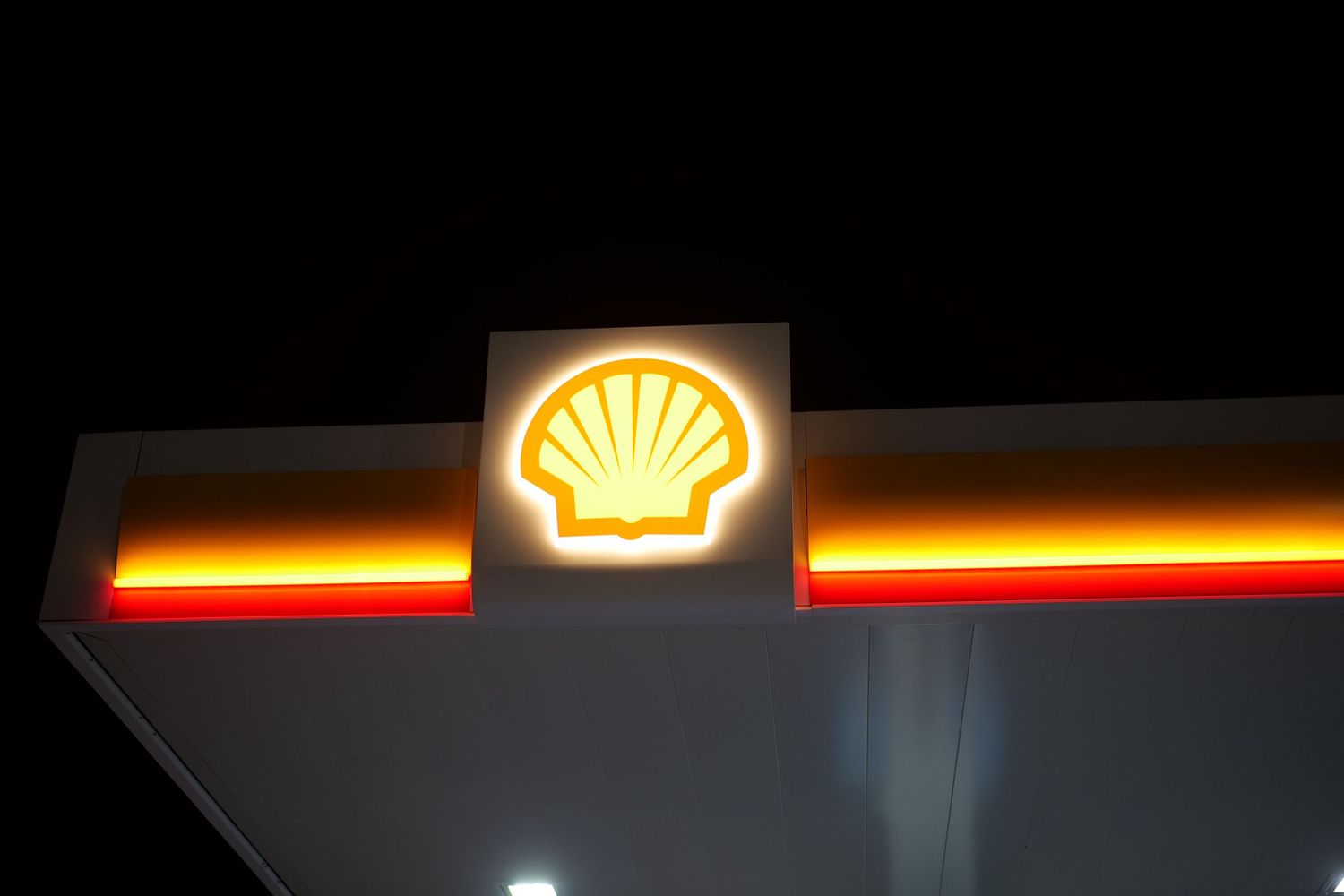 Illuminated Shell oil company logo sign glowing yellow and orange against dark night sky.