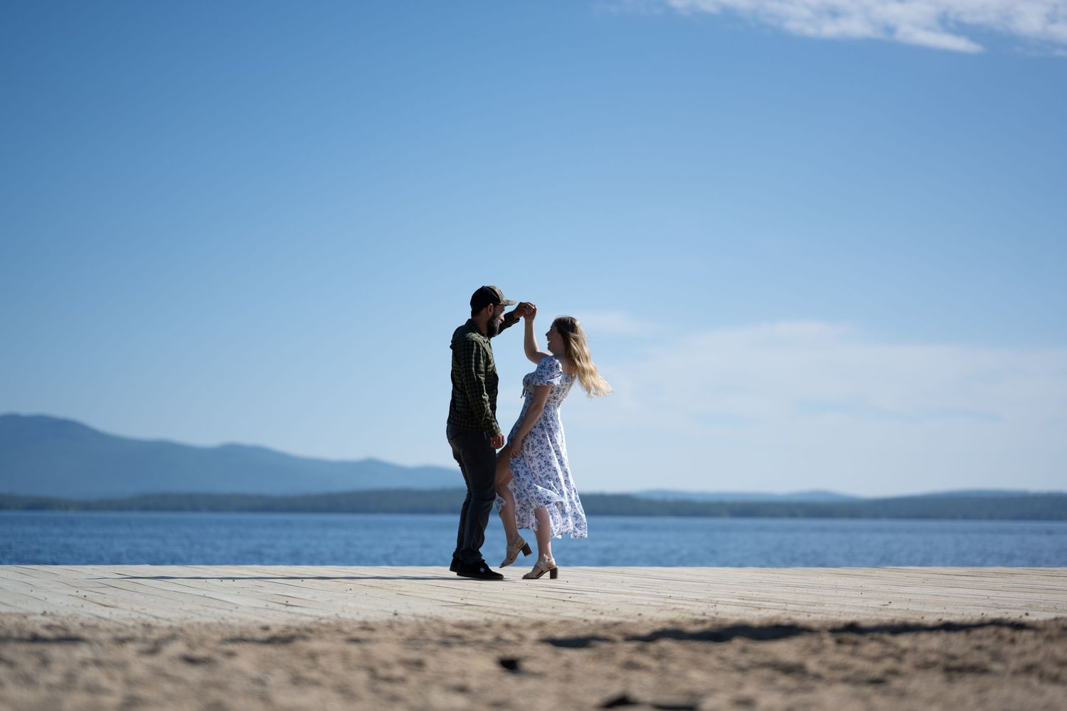 Couple dancing together on a sandy beach under a clear blue sky with mountain views.