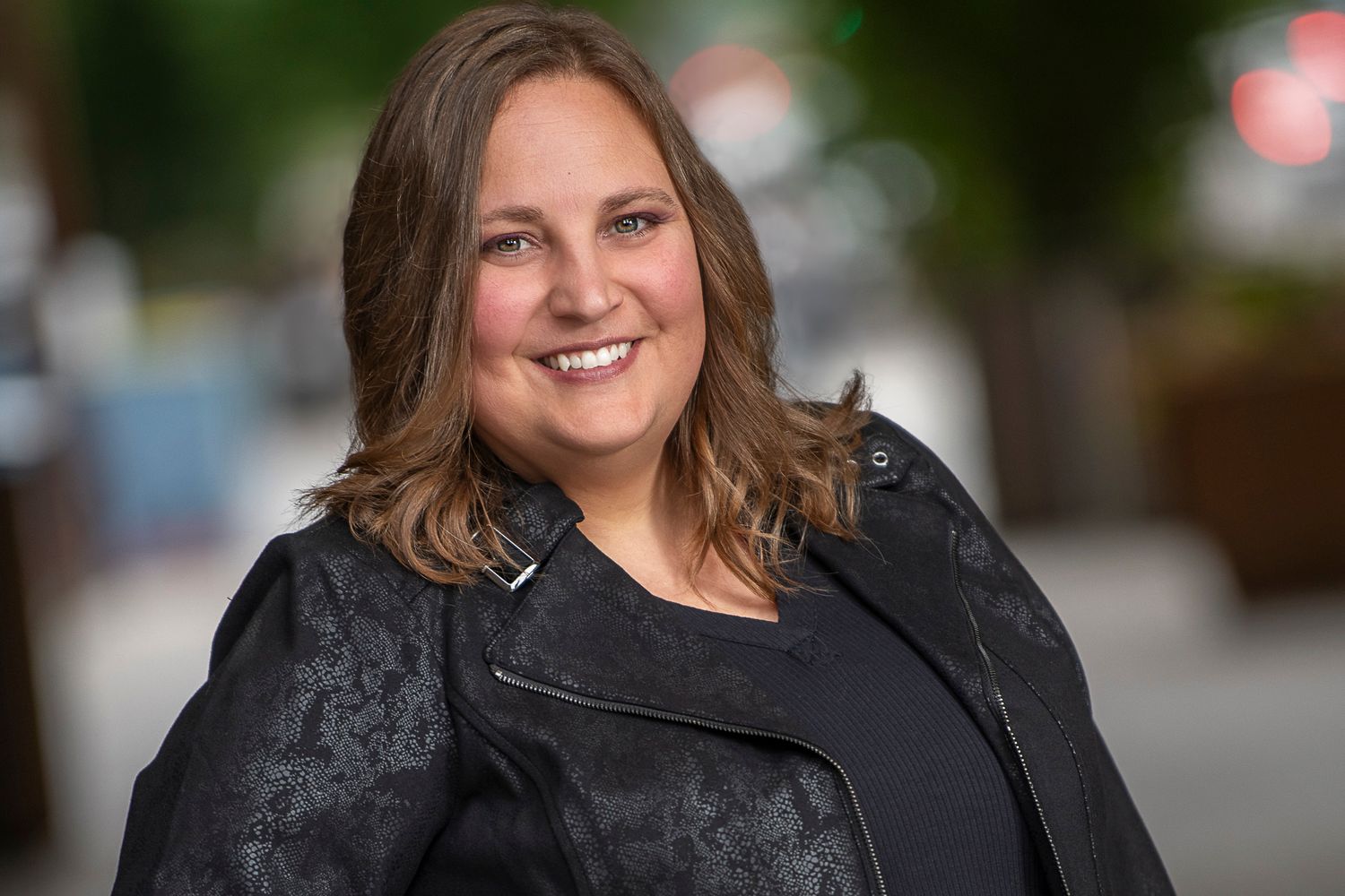Portrait shot of person in black jacket against blurred urban background.