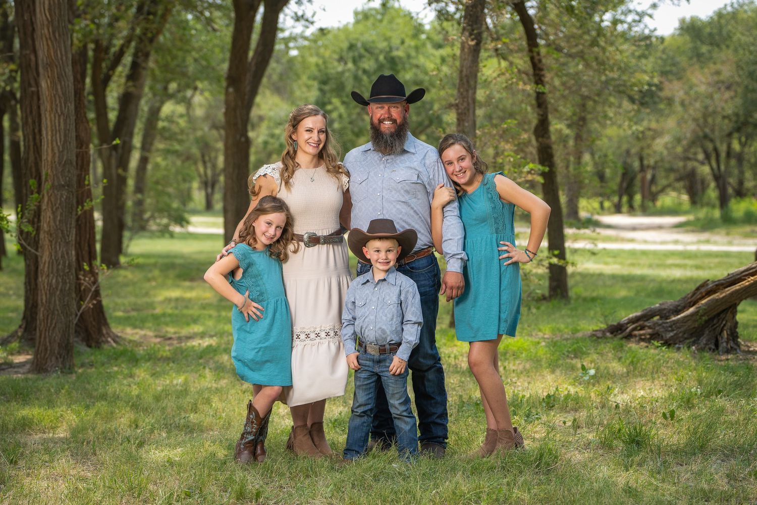 A group in coordinating blue and gray outfits poses together in a wooded outdoor setting during a photo session.