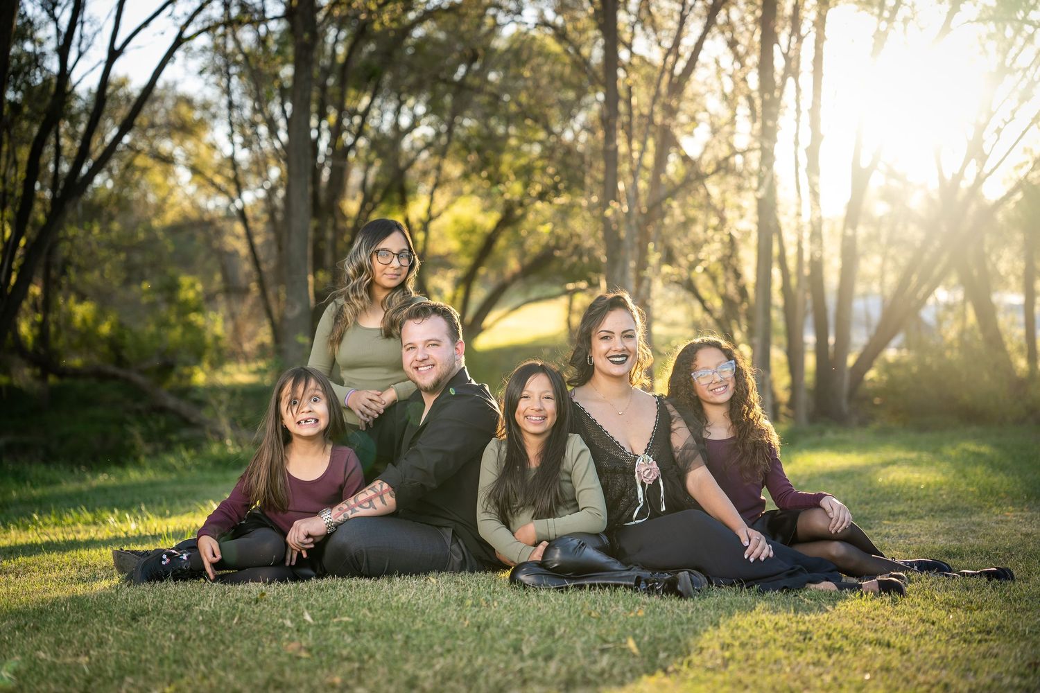 Family group poses together on grass during golden hour sunset photography session in park setting.
