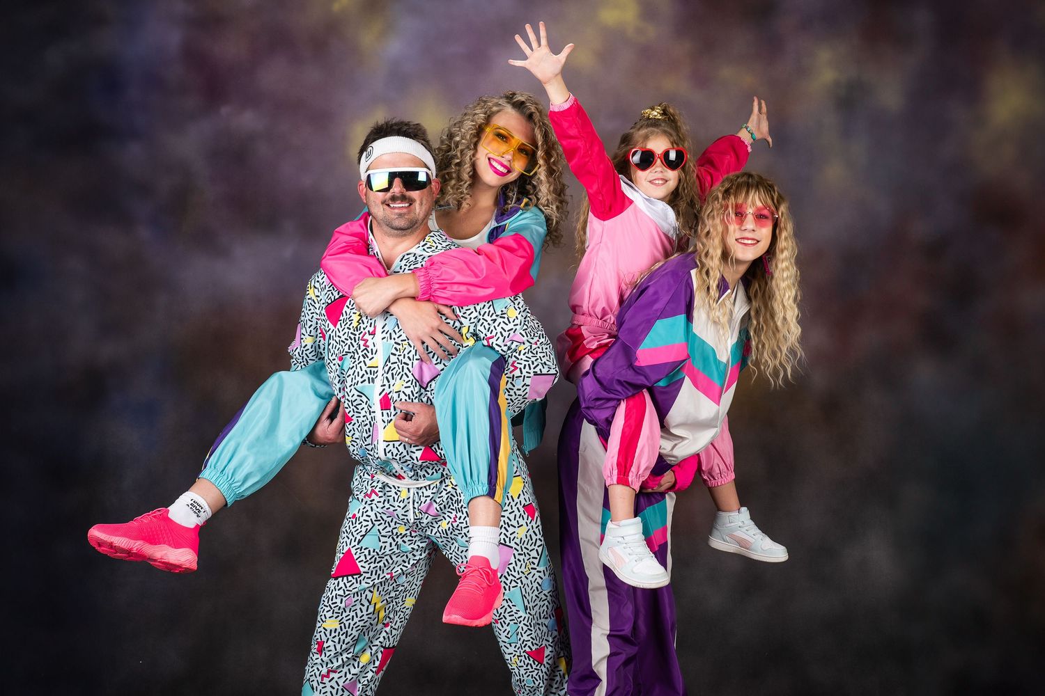 A group wearing colorful retro 80s style workout clothing poses together in dynamic dance positions.