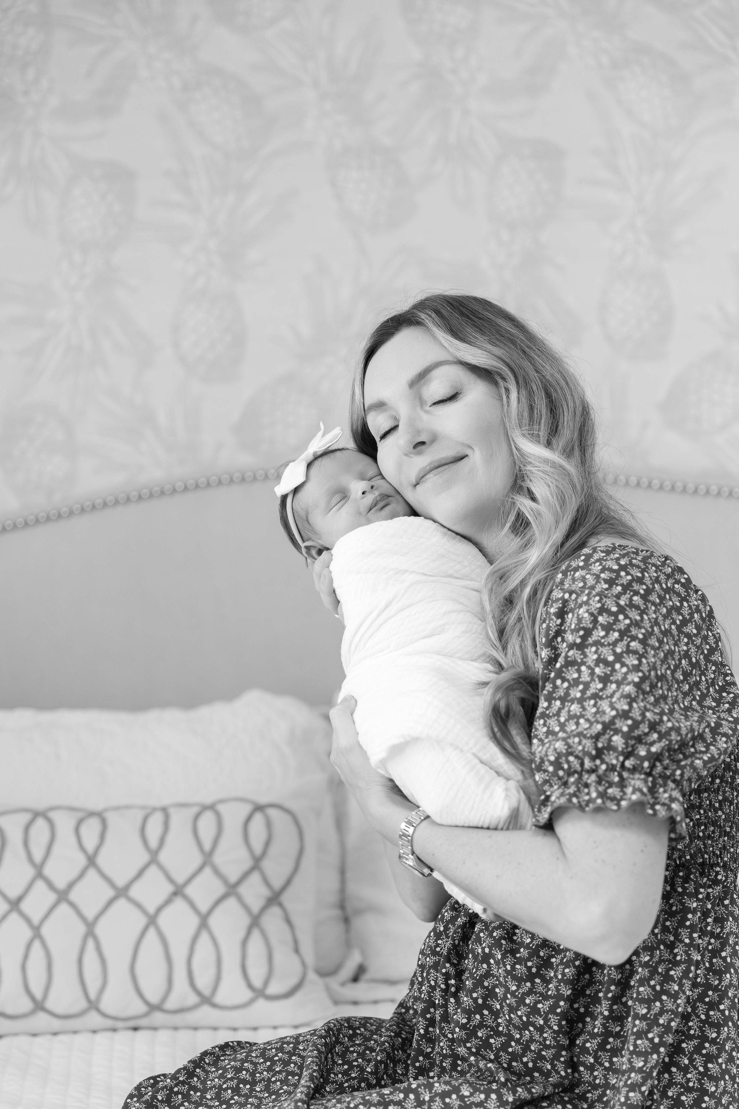 A tender moment captured in black and white as a woman holds a newborn baby in a bedroom setting.