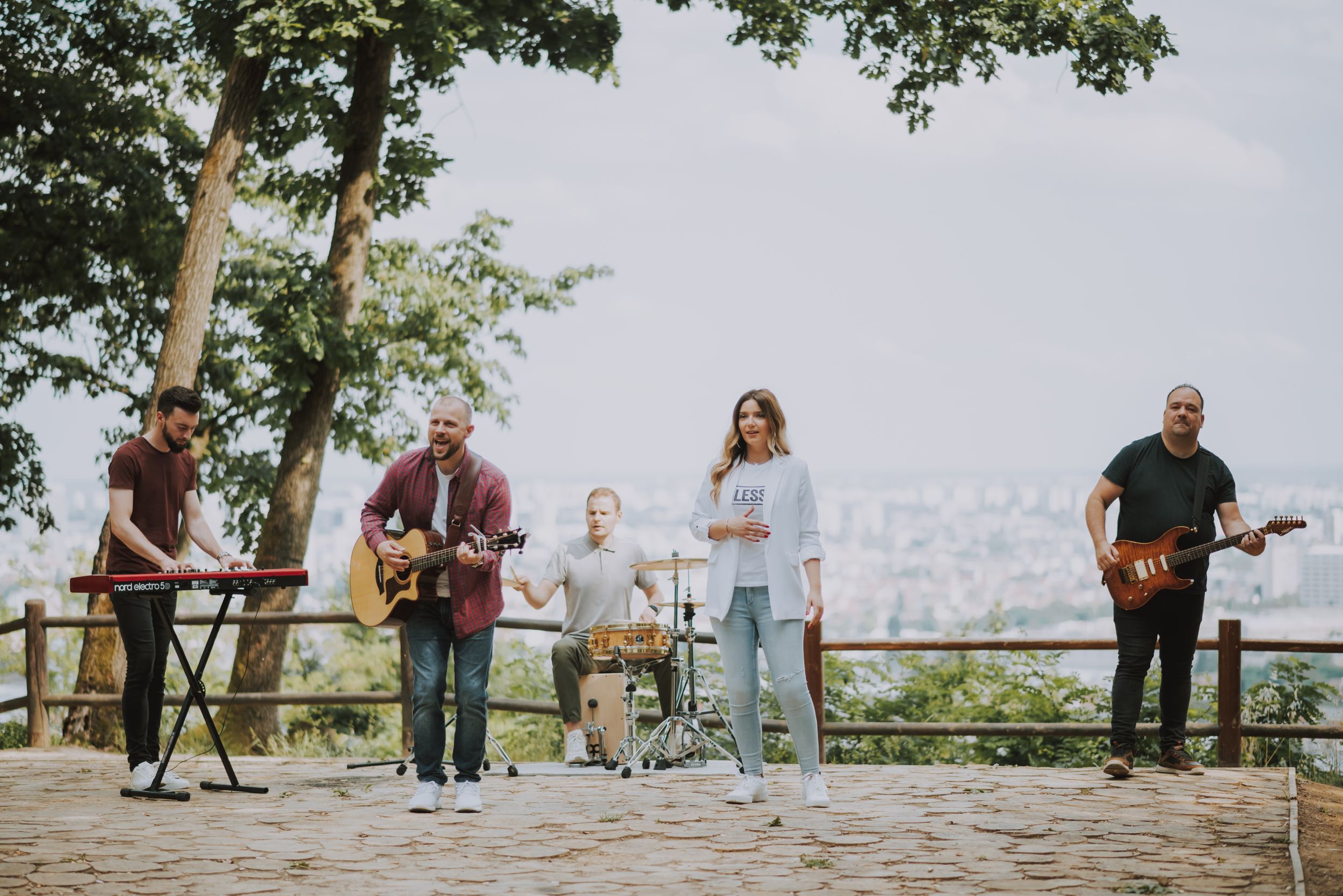 Musicians performing on outdoor stage with city panorama in background.
