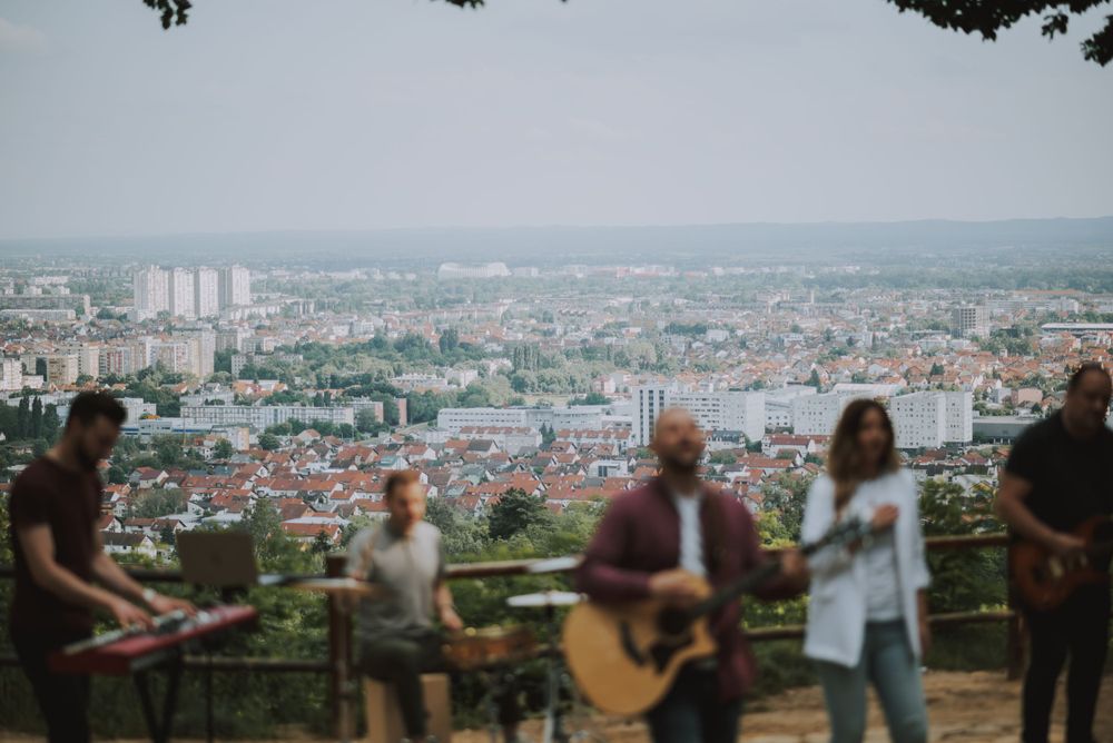 Band performing outdoor concert on hilltop overlooking cityscape.