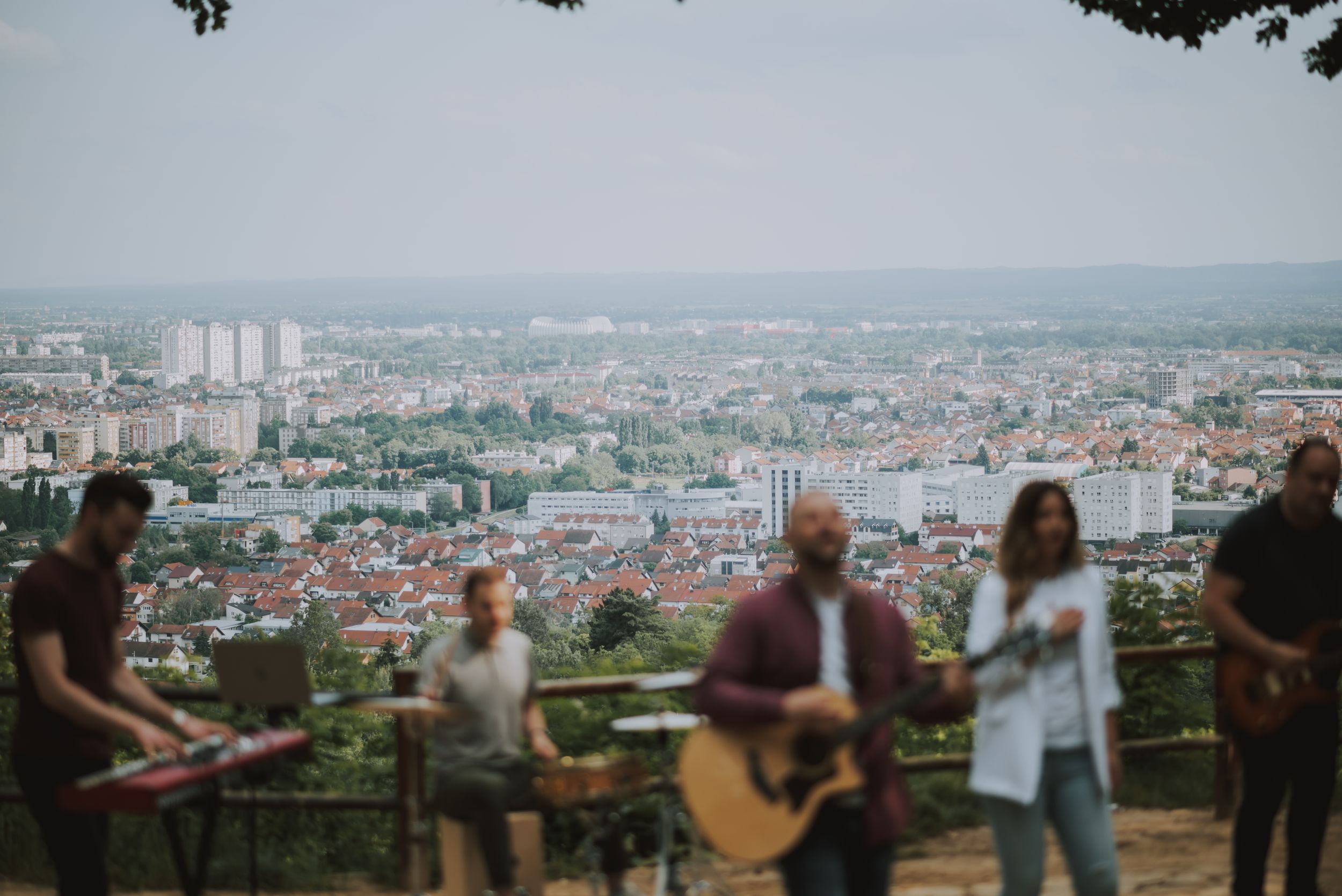 Band performing outdoor concert on hilltop overlooking cityscape.