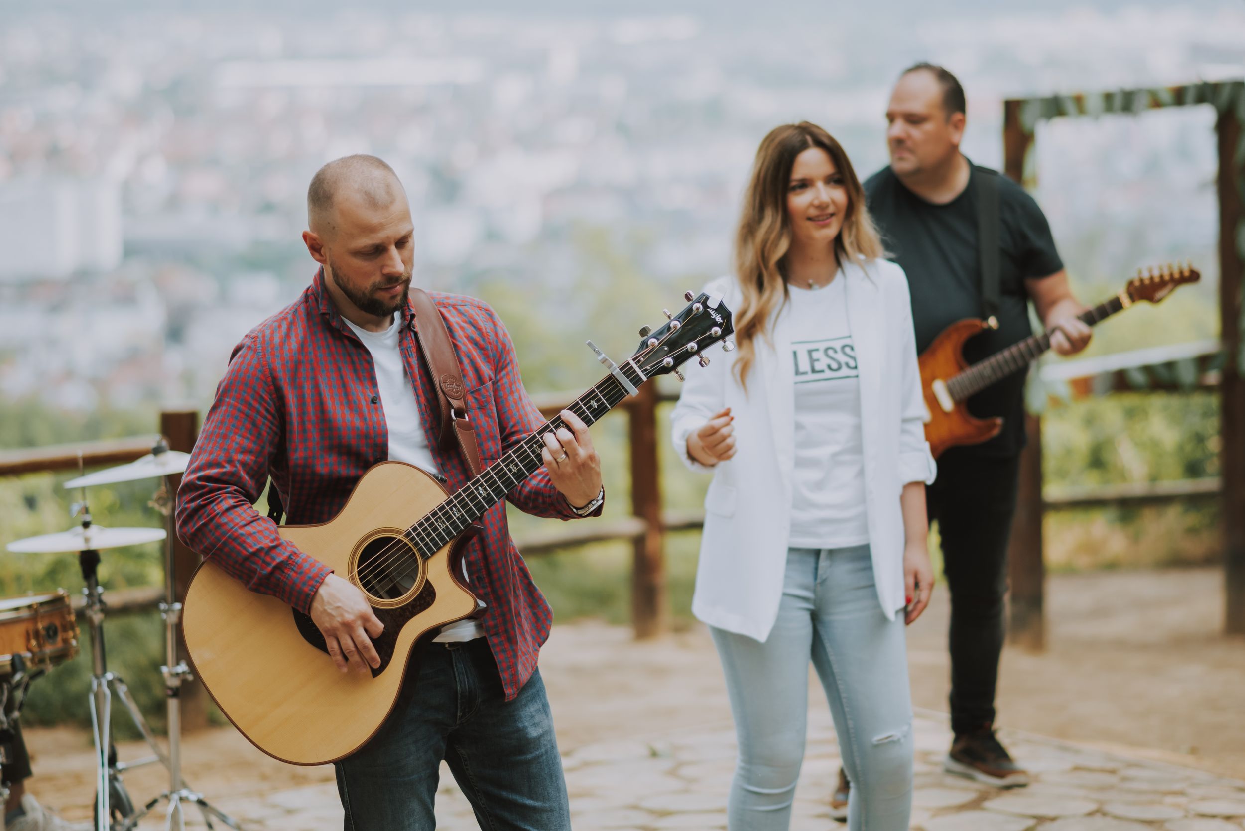 Live band performing acoustic music outdoors with scenic city view.