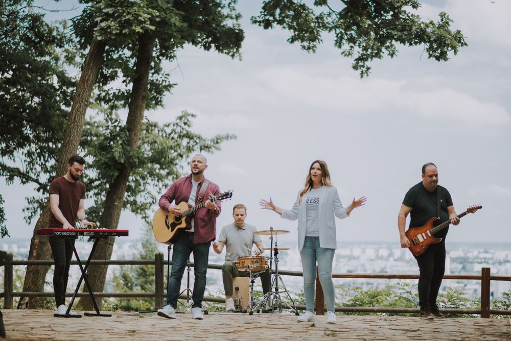 A band performs music together on a scenic overlook platform surrounded by trees with city views.