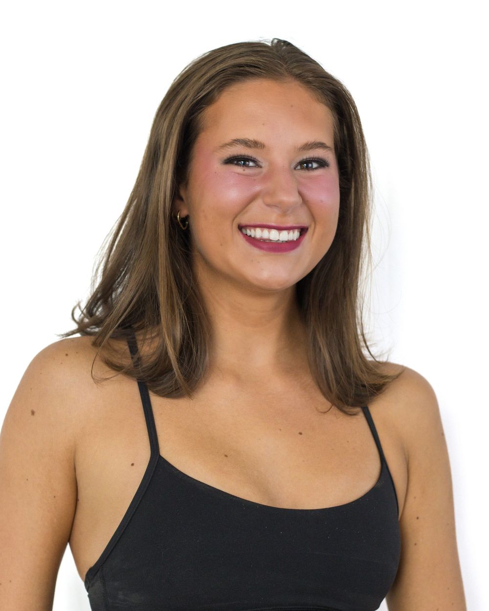A headshot of a smiling woman with brown hair wearing a black tank top against a white background.