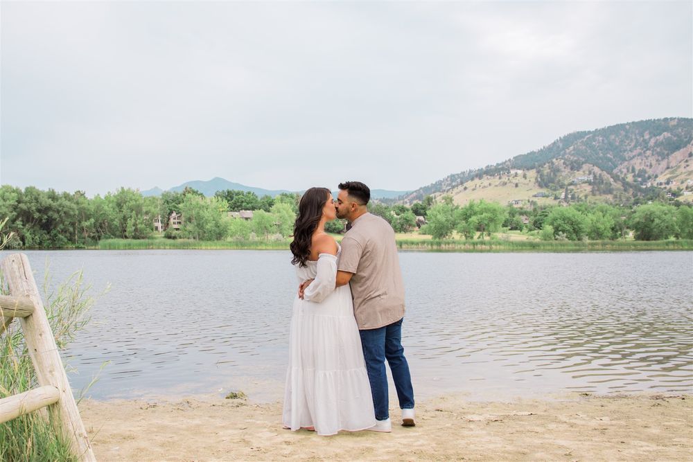 A couple enjoys a romantic moment by a serene lake with mountains in the background.