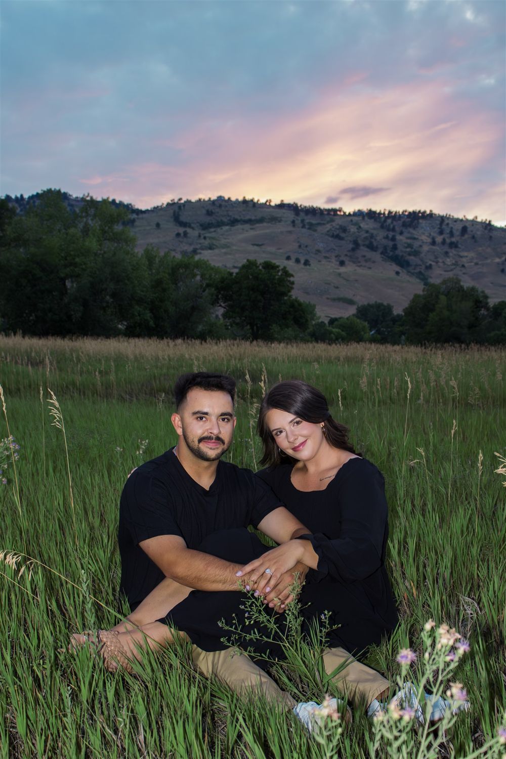 Couple in black outfits sharing intimate moments in a grassy field at sunset.