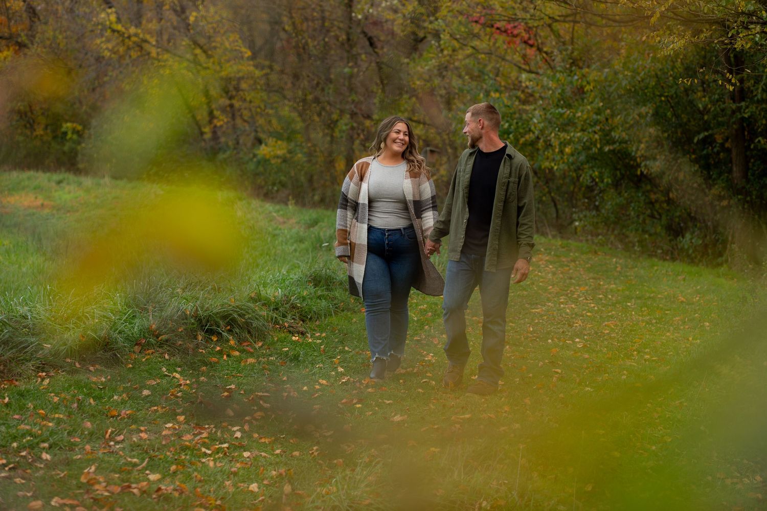 Couple walking through autumn park with fallen leaves on ground.