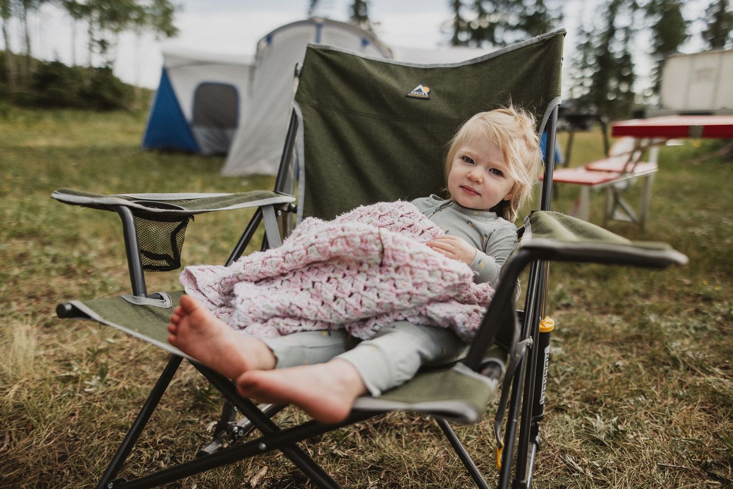 Cozy camping chair setup with blanket against outdoor backdrop.