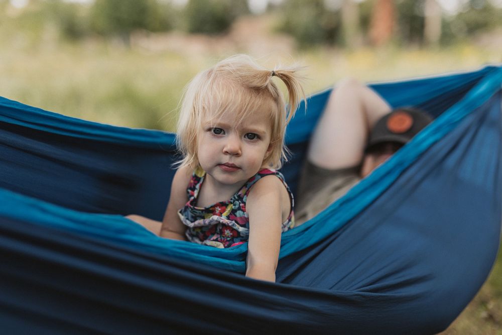 Young child relaxing in a blue camping hammock outdoors.