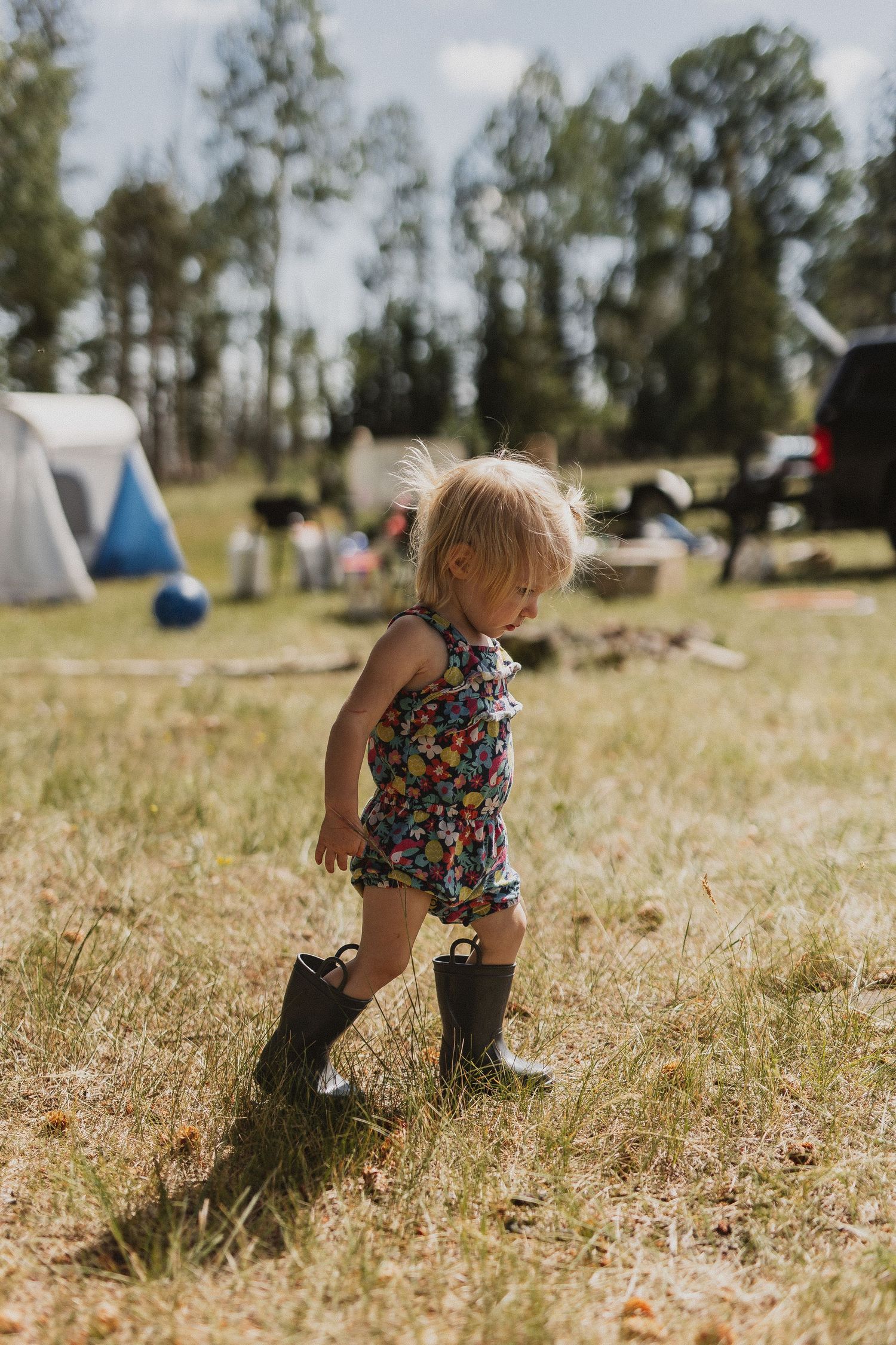 Small child wearing boots and floral outfit explores a sunny campground.