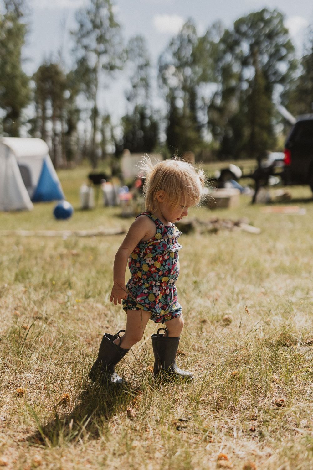 Small child wearing boots and floral outfit explores a sunny campground.