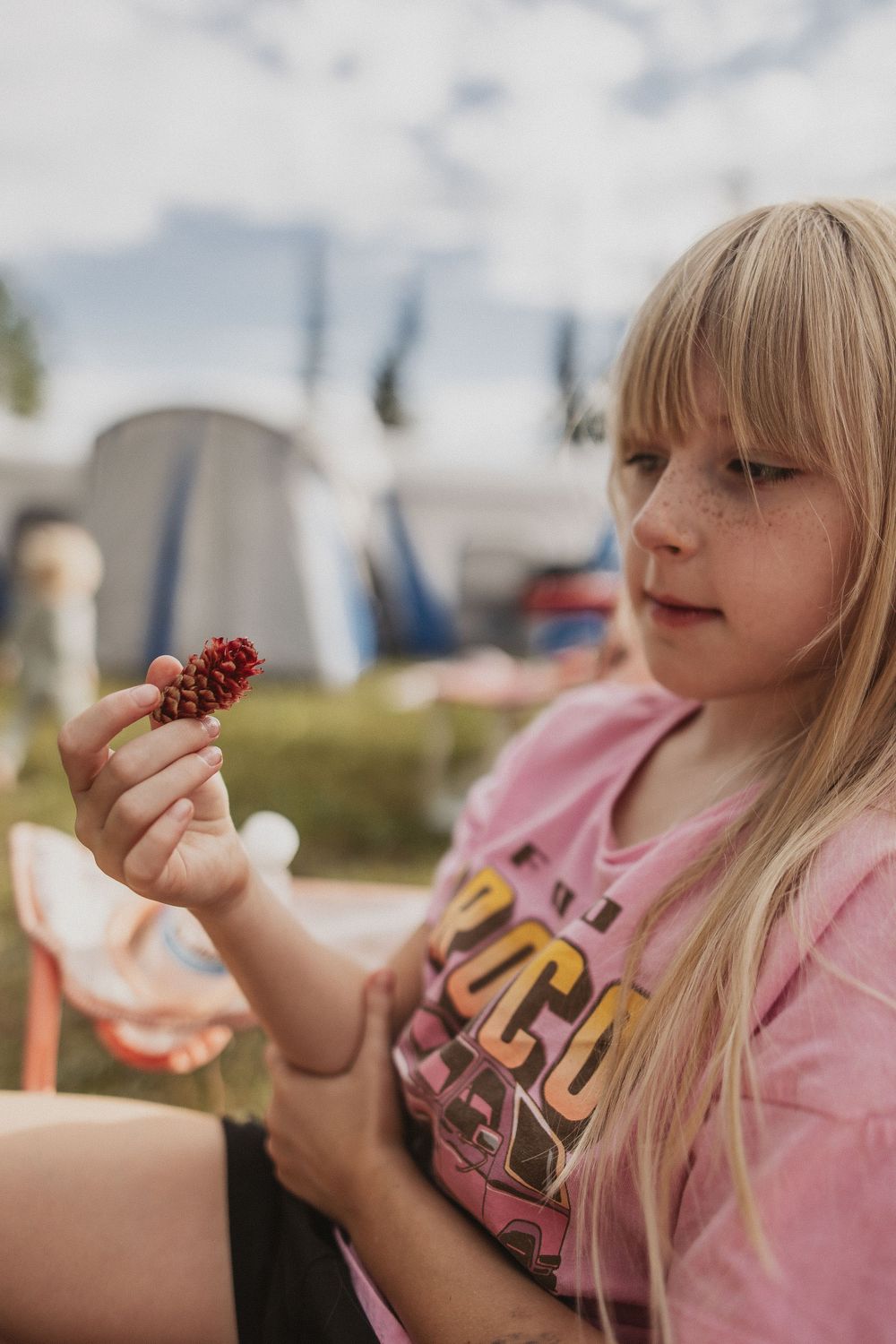 Camping scene with someone examining a pinecone outdoors.