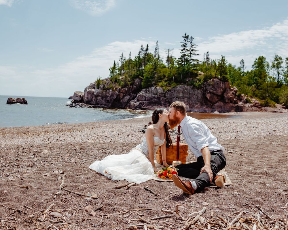 Wedding couple shares intimate moment on beach with rocky cliffs in background.