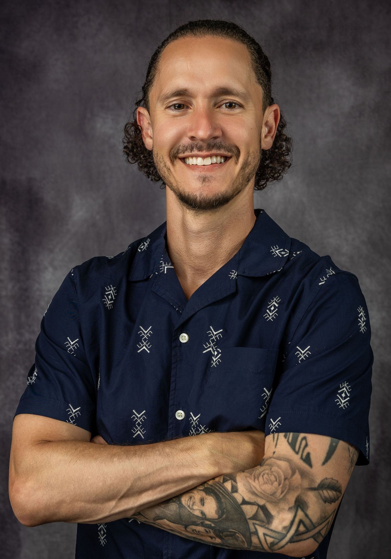 Person in navy blue patterned shirt posing against dark background in professional headshot series.