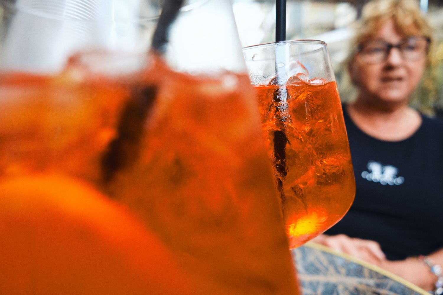Orange Aperol Spritz cocktails with ice being served at an outdoor cafe.