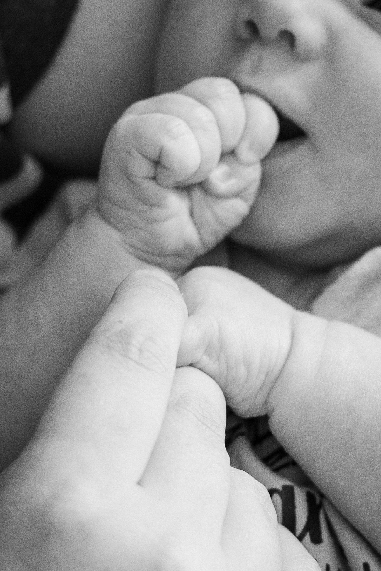 Black and white close-up of a newborn baby grasping an adult finger with tiny hands.