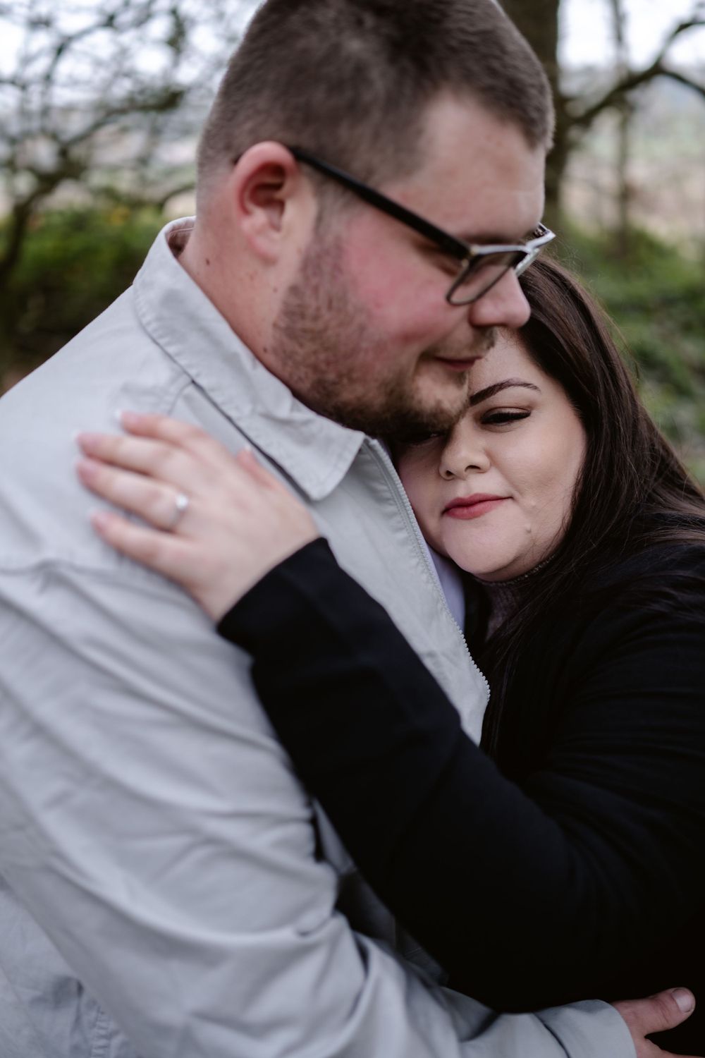 A romantic couple shares an intimate embrace outdoors with soft smiles and tender body language.