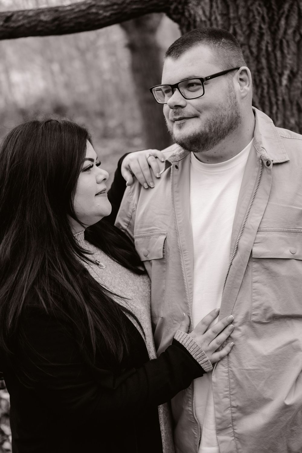 A black and white portrait of a couple sharing a tender moment while standing against a tree.