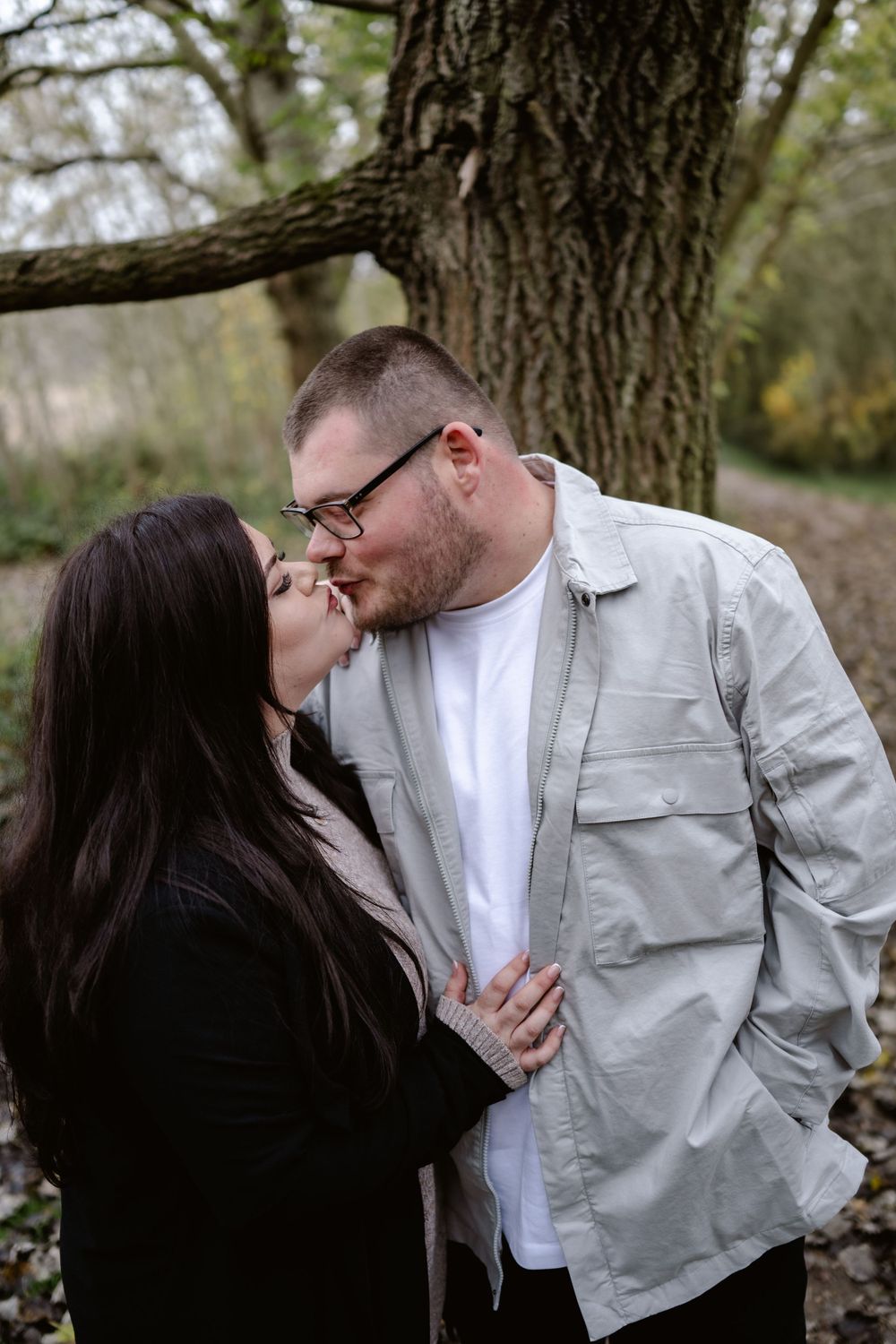 A romantic moment shared between a couple beneath a large tree in a natural outdoor setting.