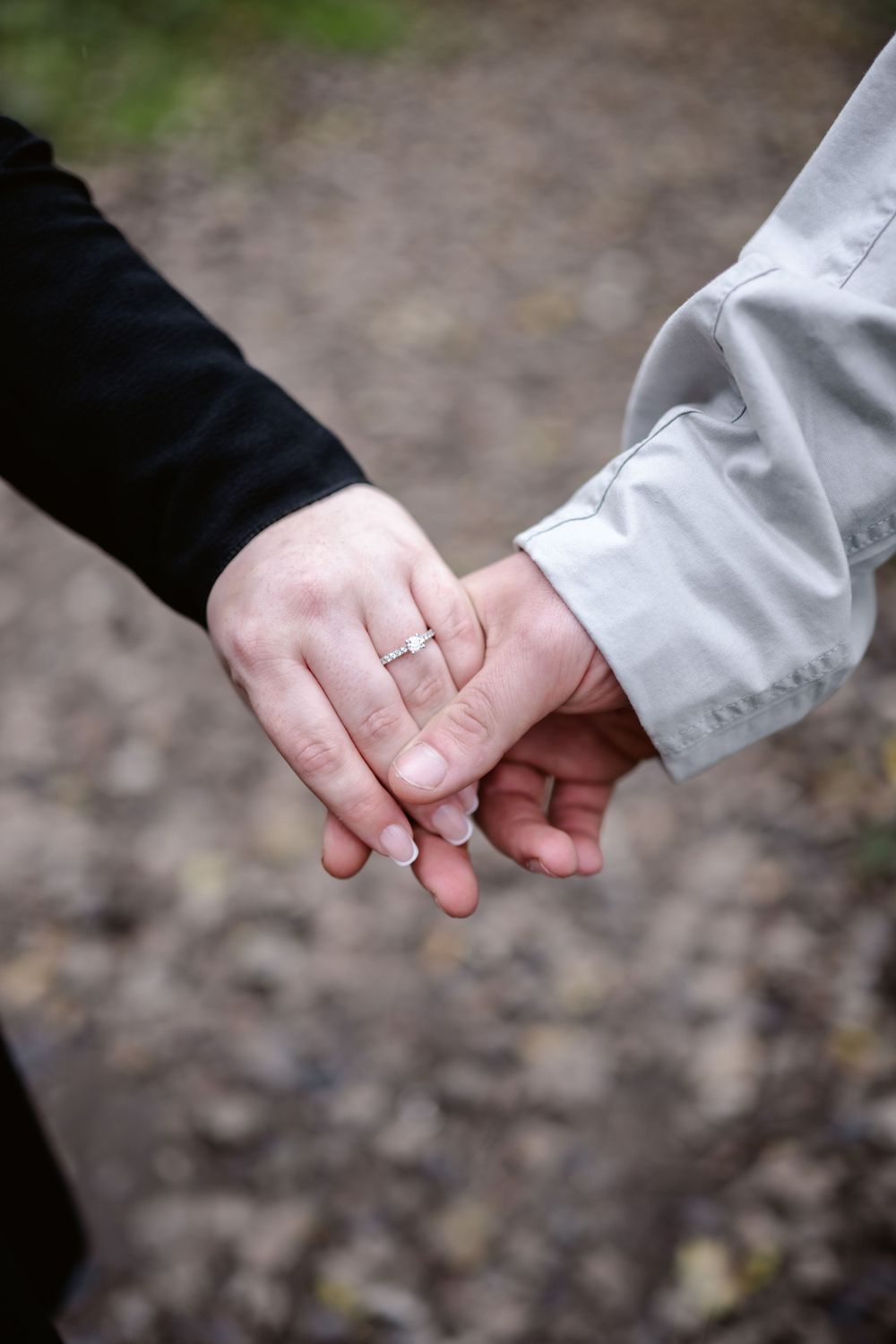 Close up of two hands gently touching, with a wedding ring visible, against a natural outdoor background.