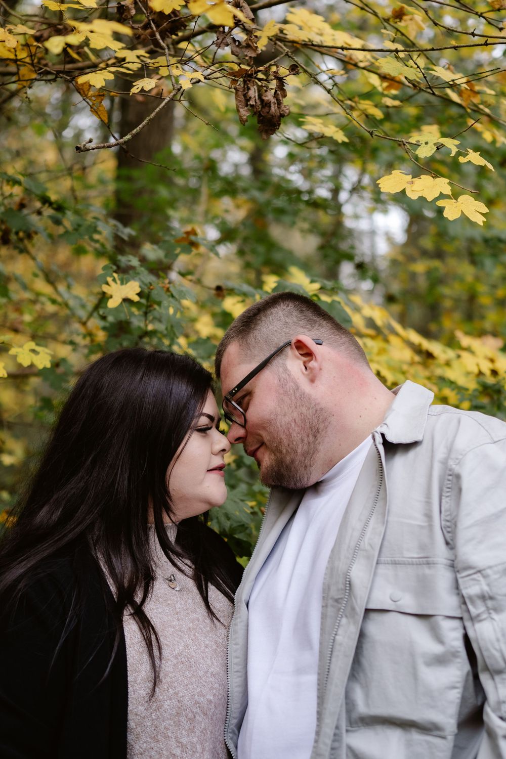 A couple shares an intimate moment beneath yellow autumn leaves in a park setting.