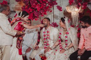 Traditional Indian wedding ceremony with vibrant red floral decor and participants wearing ornate white attire and floral garlands.
