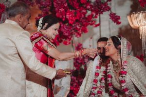 Wedding couple participating in traditional Indian ceremony rituals under bright red floral decorations.