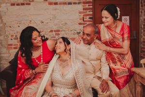 A family group wearing traditional South Asian wedding attire shares an intimate moment against a brick wall backdrop.