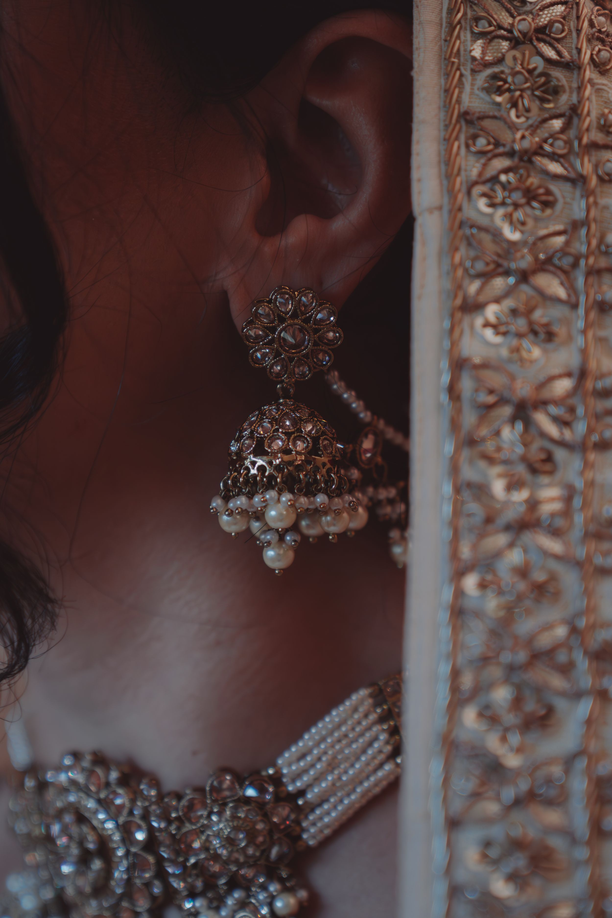 A close-up shot of an ornate crystal and pearl jhumka earring with intricate design details.