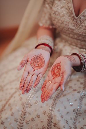 Detailed view of traditional henna designs on palms against white wedding dress fabric.