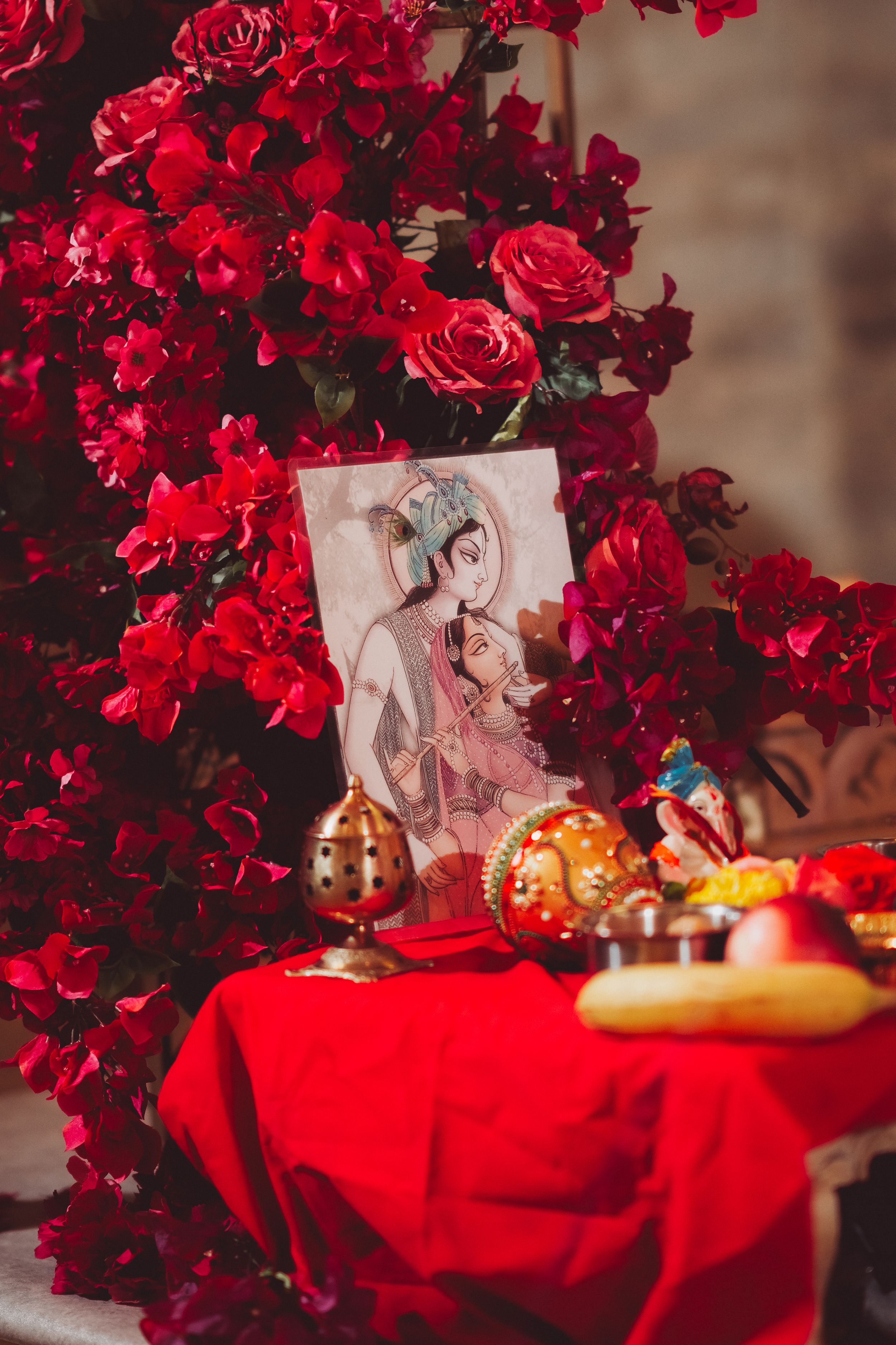 Rich red roses frame a traditional artwork display on a red-clothed table with decorative elements.
