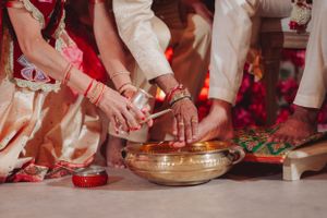Close-up of hands performing traditional Indian wedding ritual with brass bowl.
