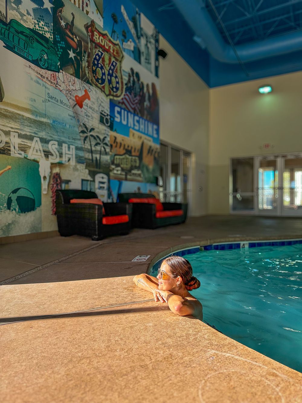 Child relaxing at the edge of an indoor pool with a colorful Route 66 Sunshine mural on the wall.