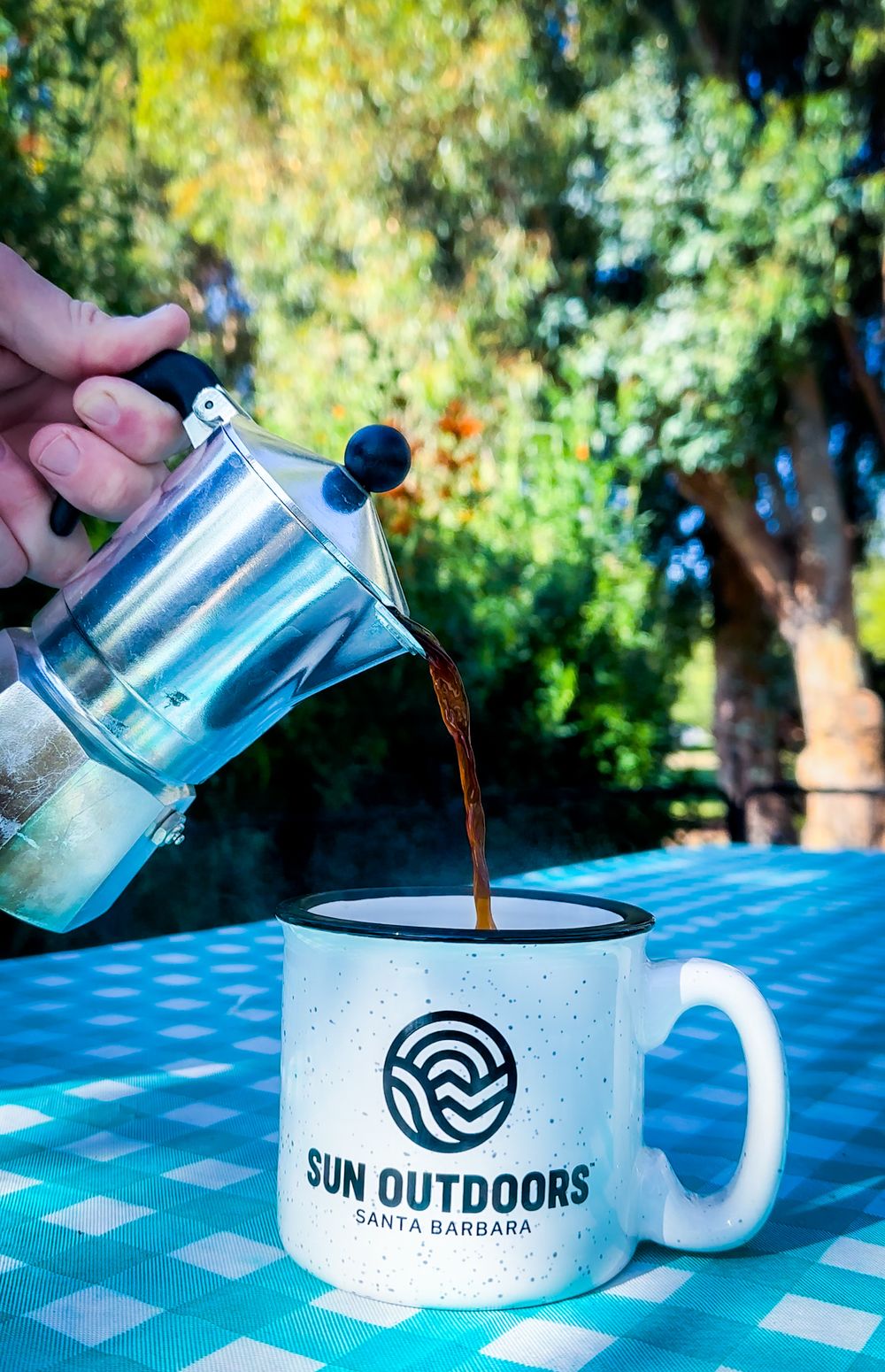Coffee being poured from a moka pot into a Sun Outdoors Santa Barbara camping mug.