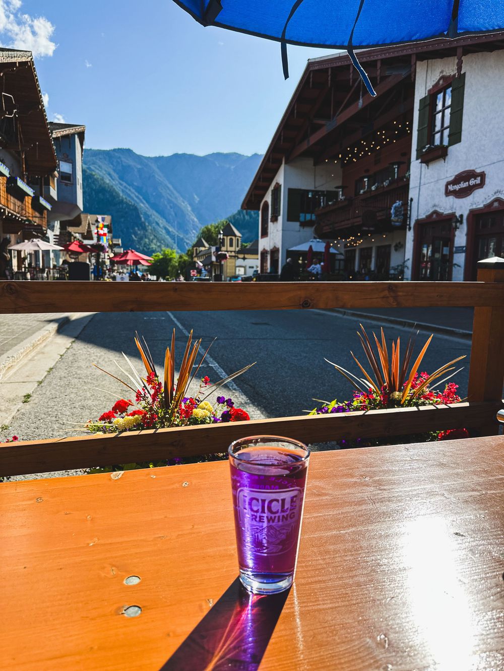 Purple craft beer glass on outdoor patio table in Bavarian-style mountain town on sunny day.