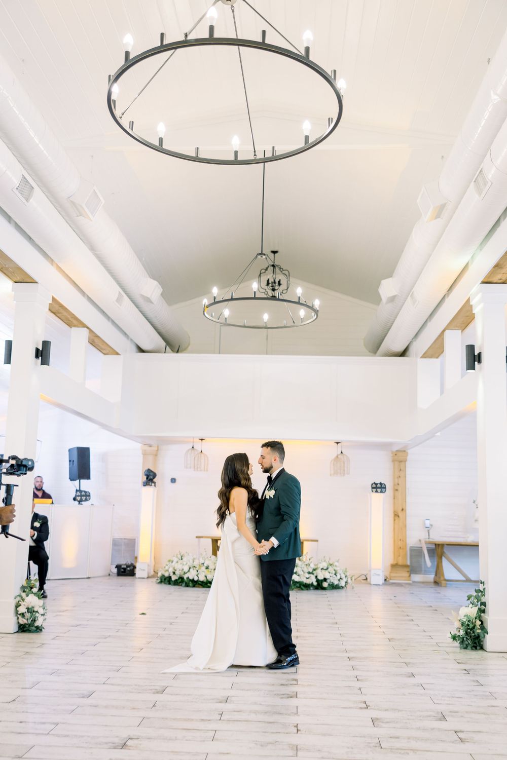 A wedding couple shares an intimate moment on a bright dance floor beneath elegant ceiling fixtures.